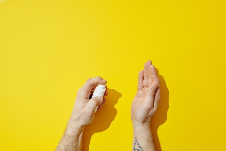 Close-up of hands using hand sanitizer spray on a bold yellow backdrop with copy space.