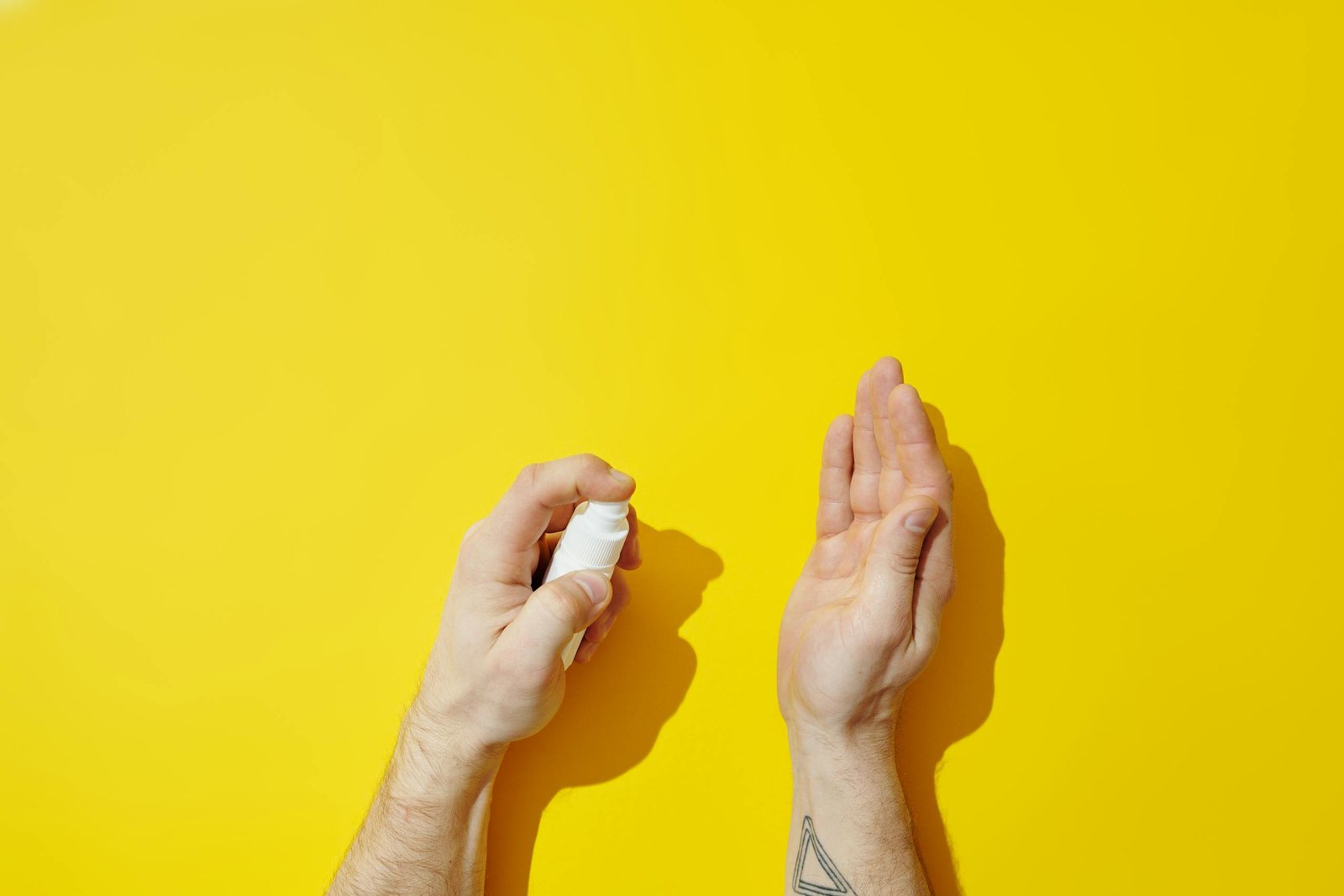 Close-up of hands using hand sanitizer spray on a bold yellow backdrop with copy space.